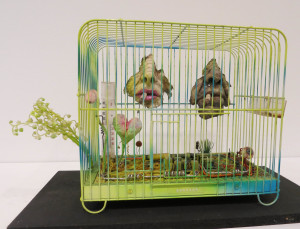 Tetsumi Kudo, Bonheur, painted cage, artificial soil, plastic flowers, cotton, plastic, polyester, resin, string, cigarettes, thermometer, Aspro tablets, circuit board, 21 x 11 x 14 inches, 1974.